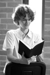 Stuart McMillen reading a book sitting at a chair. Young man reading a book on backwards-turned chair, black and white portrait.