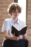 Stuart McMillen reading a book sitting at a chair. Young man reading a book on backwards-turned chair, colour portrait.